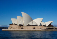 Sydney Opera House at sunset, viewed from across the harbour with the white sail-shaped roof shells visible against a clear sky.