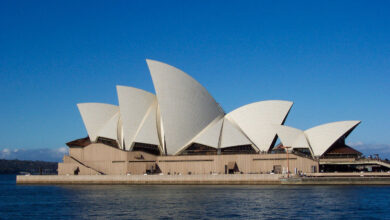 Sydney Opera House at sunset, viewed from across the harbour with the white sail-shaped roof shells visible against a clear sky.