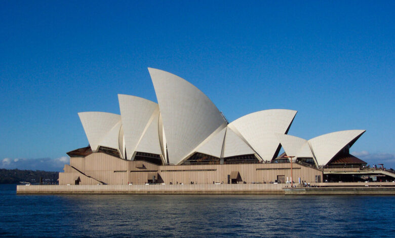 Sydney Opera House at sunset, viewed from across the harbour with the white sail-shaped roof shells visible against a clear sky.